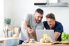 two men looking at their laptop and phone in the kitchen